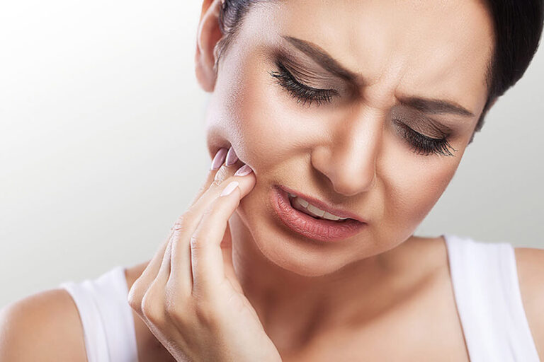 A woman in need of an emergency dental appointment, touching her jaw in pain.